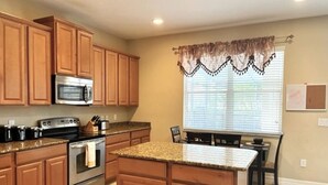 A kitchen with wooden cabinets, a stainless steel oven, granite countertops, and a window with blinds.