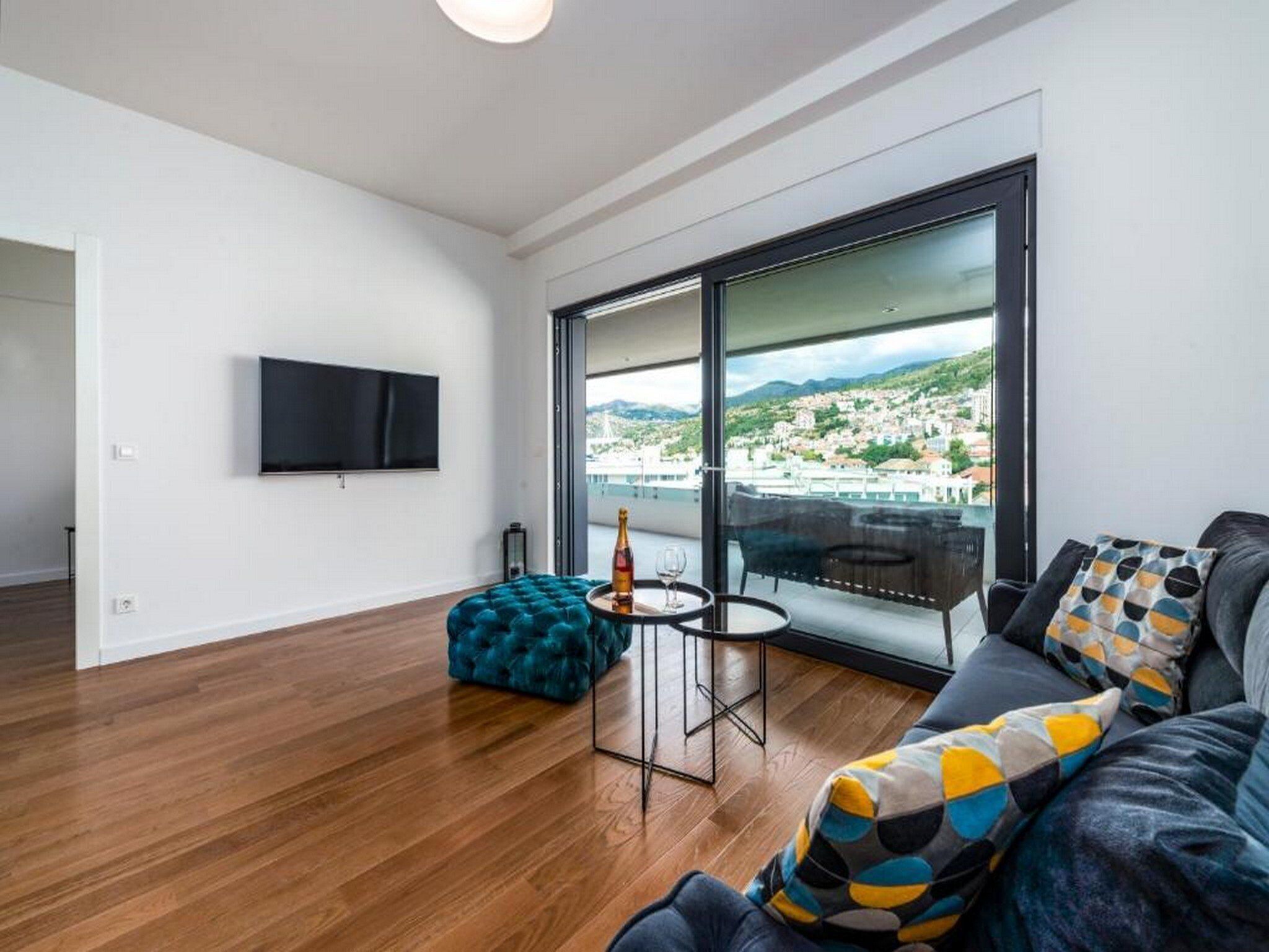 A modern living room with a large window, a flat-screen TV, and a cozy seating area.