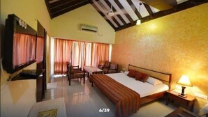 A hotel room with a bed, a desk, a chair, a TV, and a ceiling fan. - Dabchick Tourist Resort (Hodal)