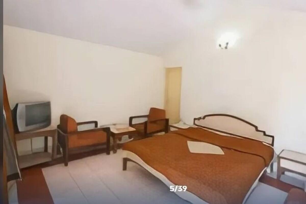 A hotel room with a bed, two chairs, a small table, and a television.