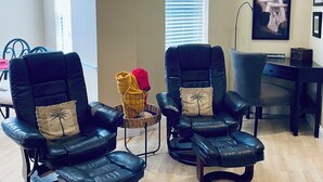A spacious room with two black leather chairs, a small table with a basket, and a desk with a chair.