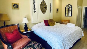 A bedroom with a large bed, a chair, a nightstand, and decorative wall art.