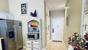 A kitchen with a stainless steel refrigerator, a microwave, and a white cabinet with drawers. There is a sign on the wall and a flower arrangement on the counter.