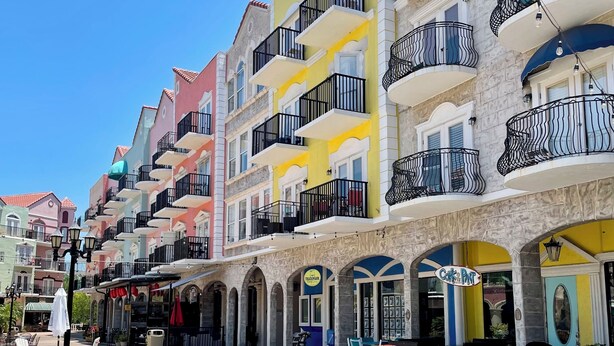 A row of colorful buildings with balconies, outdoor seating, and a sign for 'Cork & Port'.