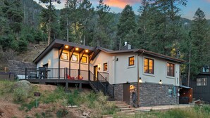 A two-story house with a deck, stone foundation, and a stone wall. - Serene Mountain View Cabin w/ Deck, Hot Tub, Fire Pit, Forest & Peak Retreats (Cascade-Chipita Park)
