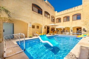 A swimming pool with lounge chairs and umbrellas, surrounded by a stone building with arched windows. - 300y/o Gozo Country Villa: pool, games, sleeps 14 (Sannat)