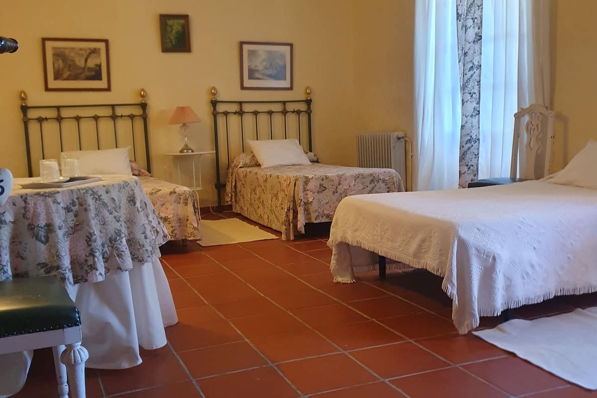 Habitación de hotel con dos camas individuales, una mesita con una silla, ventilador de techo y radiador.