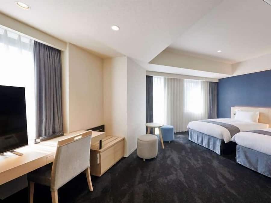 Habitación de hotel con escritorio, silla, dos camas, televisor y una mesita.