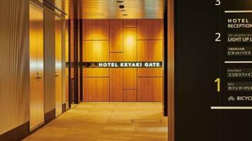 En hotellreception med en dörr i trä som är märkt med texten ”HOTEL KEYAKI GATE”, och en informationsskylt på höger sida.