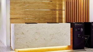A reception desk with a marble top, wooden paneling, and a black security kiosk. - Hotel Keyaki Gate Tokyo Fuchu (Fuchu)