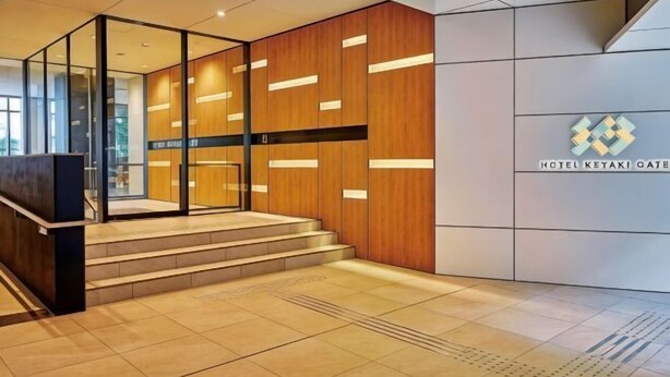 A hotel lobby with a reception desk, a staircase, and a logo on the wall. - Hotel Keyaki Gate Tokyo Fuchu (Fuchu)