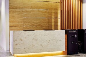 A reception desk with a marble top, a wooden panel wall, and a black electronic device to the right. - Hotel Keyaki Gate Tokyo Fuchu (Fuchu)