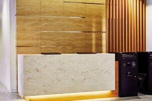 A reception desk with a marble top, a wooden panel wall, and a black electronic device to the right.