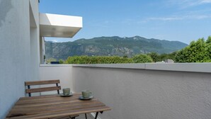 Un balcón con una mesa de madera y dos tazas, con vistas a un paisaje montañoso.