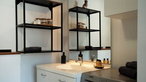 Un baño moderno con un lavabo blanco, estanterías negras, un espejo y una lavadora Valberg.