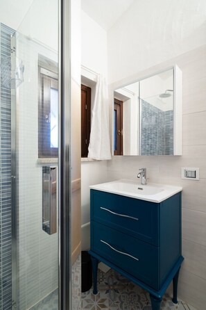 Ein Badezimmer mit Duschkabine aus Glas, einem weißen Waschbecken mit blauem Unterschrank und einem Spiegel über dem Waschbecken.