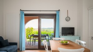 Una habitación con una mesa de comedor, sillas, un televisor y vistas a la vegetación exterior.