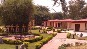 A courtyard with a central seating area, surrounded by trees and a building with a red roof. - Design galleries complex (Faridabad)