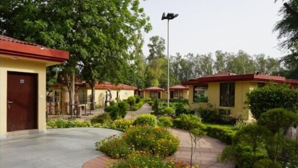 A courtyard with multiple buildings, each with a red roof and yellow walls, surrounded by well-maintained greenery and a paved walkway. - Design galleries complex (Faridabad)