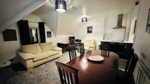 A compact living space with a dining table, a sofa, a kitchen area, and a ceiling light fixture. - 1 Luxe Exec Bedroom Apt Derby (Derby)