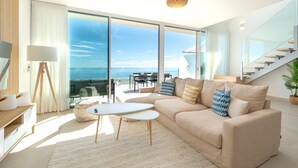 Una sala de estar moderna con un sofá grande, una mesa de centro y vistas al mar a través de ventanas de gran altura.