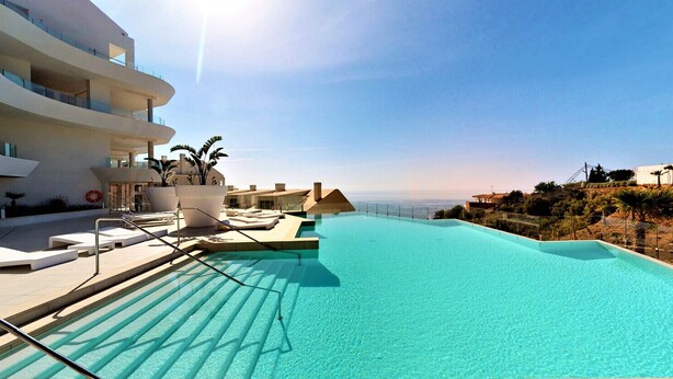 Un hotel moderno con una amplia piscina infinita, asientos al aire libre y vistas a la costa.