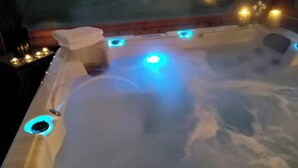 Un bain à remous avec des lumières LED bleues, une serviette et des bougies sur une terrasse en bois.