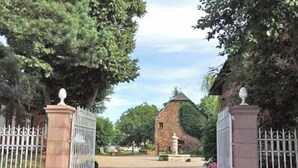 Une entrée fermée par un portail, avec un chemin pavé menant à un bâtiment en pierre surmonté d’une tour.