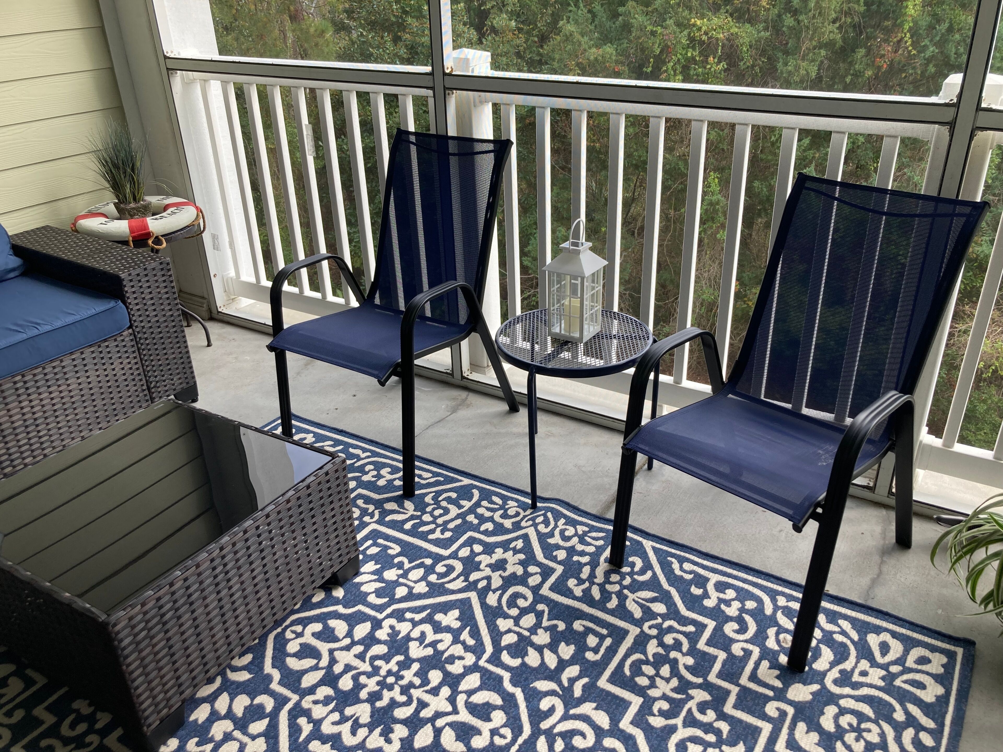 Un balcone con due sedie azzurre, un tavolino e un tappeto decorativo.
