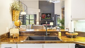 Une cuisine moderne avec un plan de travail en bois foncé, un évier intégré et un coin repas comprenant un canapé et un téléviseur en arrière-plan.