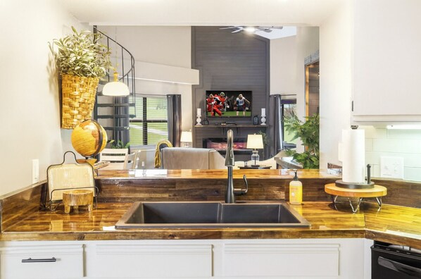 A modern kitchen with a dark wood countertop, a built-in sink, and a dining area with a sofa and a TV in the background. - Family Fun Resort. Enjoy Pools, Hot Tub, Golf, Game Room, Fishing, Karaoke (Branson)