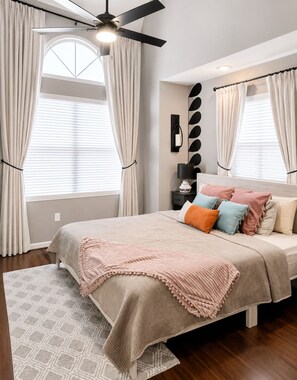 A bedroom with a bed, curtains, a ceiling fan, a wall-mounted lamp, and a patterned rug. - Family Fun Resort. Enjoy Pools, Hot Tub, Golf, Game Room, Fishing, Karaoke (Branson)