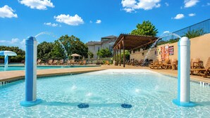 Une piscine avec des chaises longues, un espace de détente couvert et un bâtiment en arrière-plan.