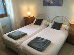 Two single beds with simple headboards and nightstands, each with a lamp, are flanked by a wall-mounted painting.