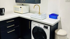 Een kleine keuken met een magnetron, spoelbak en wasmachine.