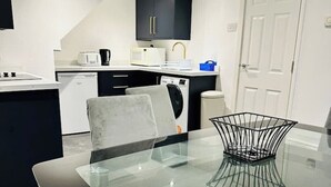 Een moderne keuken met een zwart aanrecht, een glazen eettafel met een metalen decoratie en een witte deur op de achtergrond.