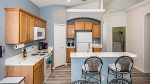 A modern kitchen with wooden cabinets, a white refrigerator, and a central island with bar stools. - 'Sunshine State of Mind' South Facing Pool & Spa (Clermont)