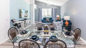 A dining area with a glass table, wicker chairs, and a blue sofa in the background. - 'Sunshine State of Mind' South Facing Pool & Spa (Clermont)