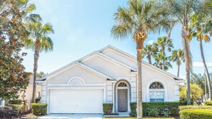 A single-story house with a white garage door, a front entrance with a small porch, and a well-maintained lawn with palm trees. - 'Sunshine State of Mind' South Facing Pool & Spa (Clermont)
