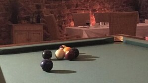 A billiards table with balls and a cue stick, set against a brick wall with a fireplace and seating area. - Chambres Familiales Ravel - Domaine du Mas Naut (Conques-en-Rouergue)