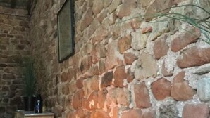 A rustic stone-walled room with a wooden bench, a small table with a candle, and a framed picture on the wall. - Chambres Familiales Ravel - Domaine du Mas Naut (Conques-en-Rouergue)