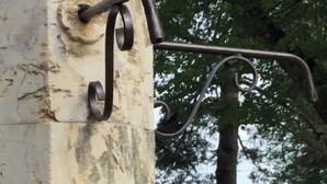 A wine bottle and glass on a stone ledge with a metal railing and a view of trees and hills. - Chambres Familiales Ravel - Domaine du Mas Naut (Conques-en-Rouergue)