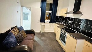 Un espacio habitable compacto con kitchenette, un sofá y vista a través de una puerta.
