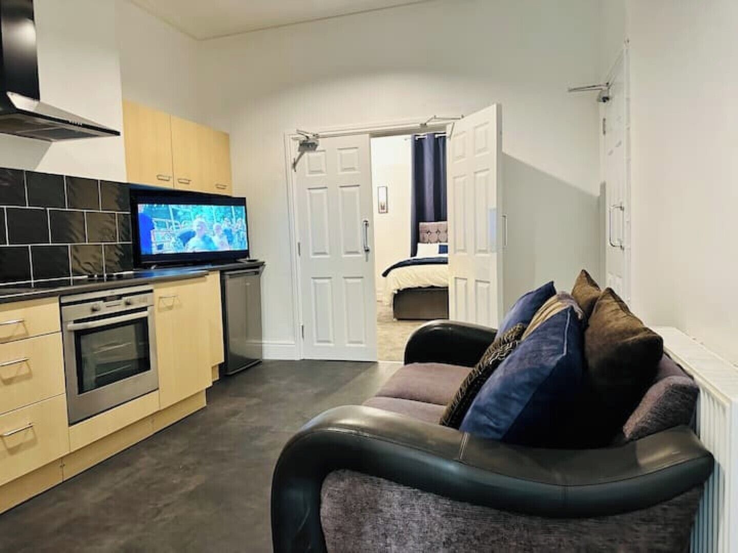 Una cocina moderna con un televisor, un sofá con cojines y una puerta que da a un dormitorio.