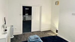 Un dormitorio con una puerta blanca, una mesita de noche pequeña con una lámpara, una colcha azul y una alfombra oscura.