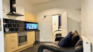 Un espacio habitable pequeño con kitchenette, un sofá de cuero y un televisor.