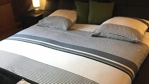 A neatly made bed with striped bedding, a dark headboard, and a wall-mounted light fixture. - Chambre D'hôtes Référence® "La Valse" + Jacuzzi (Conques-en-Rouergue)