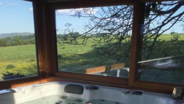 A hot tub with a bottle of champagne and two glasses, overlooking a green landscape. - Chambre D'hôtes Référence® "La Valse" + Jacuzzi (Conques-en-Rouergue)