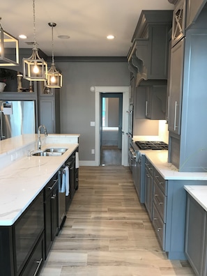 A modern kitchen with a central island, dark cabinetry, and a light-colored countertop. - Luxury Vacation Home -Lake Winnipesaukee with 50' Dock w outdoor firepit. (Meredith)