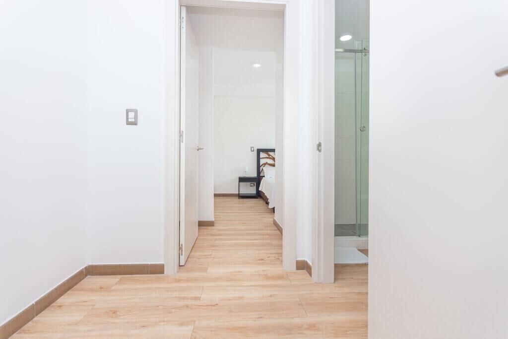 A hallway with wooden flooring and white walls, leading to a room with a glass door.
